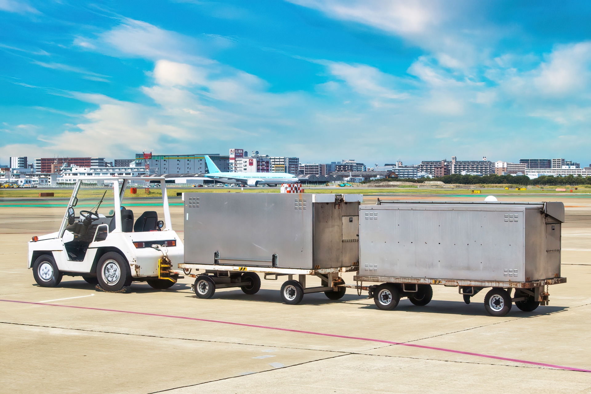 空港の滑走路付近で航空貨物用コンテナを牽引するトーイングトラクター